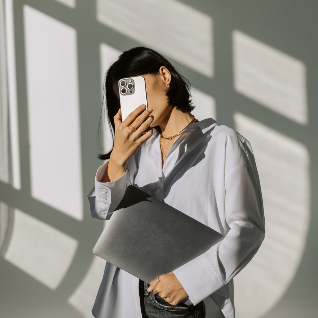 Person holding a phone and a gray bag against a wall with sunlight casting shadows
